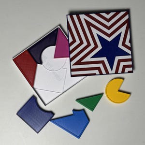 May include: A colorful puzzle with geometric shapes and a star-patterned box. The puzzle pieces include a blue, green, and yellow shapes, along with a white box containing other shapes. The box has a red, white, and blue star design.