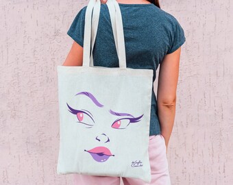 May include: A white tote bag featuring a cartoon face print. The face has purple eyebrows, pink eyes, and a purple mouth. The text "Kayla Casale" is printed in the bottom right corner of the bag.