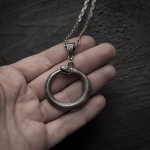 May include: A silver snake pendant necklace with a snake forming a circle. The snake is detailed with scales and has a textured finish.