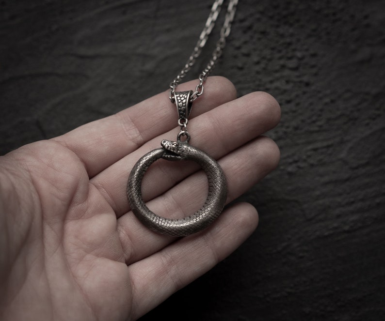 May include: A silver snake pendant necklace with a snake forming a circle. The snake is detailed with scales and has a textured finish.