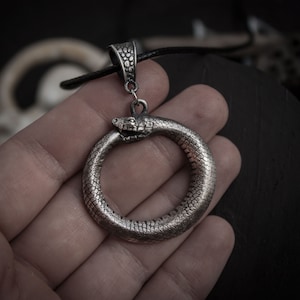 May include: Silver pendant necklace featuring a snake forming a circle with its tail in its mouth. The snake is detailed with scales and has a realistic head.