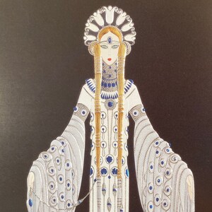 May include: A white gown with a long train and a blue and gold beaded design. The gown is worn by a woman with long blonde hair and a blue and gold crown. The background is black.