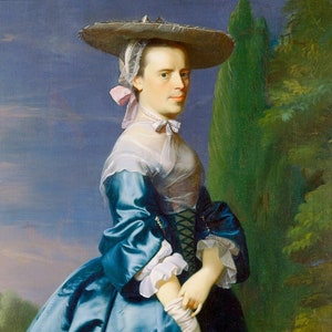 May include: A woman in a blue dress and white lace collar stands in a garden setting. She wears a wide-brimmed hat with a pink ribbon and holds a white glove in her right hand.