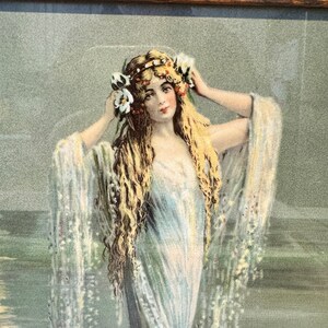 K&ouml;nnte beinhalten: Eine Vintage-Illustration einer Frau mit langen blonden Haaren, die ein wei&szlig;es Kleid und eine Blumenkrone tr&auml;gt. Sie steht vor einem gr&uuml;n-blauen Hintergrund, der an Wasser erinnert.