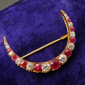 Puede incluir: Un broche en forma de media luna hecho de oro amarillo, con un patrón alterno de rubíes rojos y diamantes blancos transparentes de talla redonda a lo largo del marco curvo, con un fino alfiler de oro en la parte posterior.