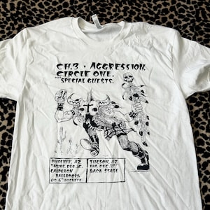 May include: White t-shirt featuring a black and white graphic of a horned figure with a skull and a beer can. The shirt also has text that reads "CH.3, AGGRESSION, CIRCLE ONE, SPECIAL GUESTS." and concert details.