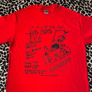 May include: Red t-shirt with black text and graphic. The text reads "LA.s First All Skate Gig! with: The Big Boys J.F.A. Agression Faction Ill Repute Tales + Tetrot Friday 7:30 May 18th Stardust Ballroom 5612 Sunset Blvd. For Info 464-2205". The graphic is a skeleton on a skateboard.