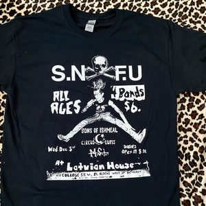 Könnte beinhalten: Schwarz-weißes Grafik-T-Shirt mit einem Punkrock-Band-Poster für S.N.F.U. mit dem Text "Alle Altersgruppen" und "4 Bands 6$". Das Poster enthält auch das Datum "Mi. 3. Dez." und den Ort "Im Latvian House 491 College St. W., 1 1/2 Blocks westlich von Bathurst."