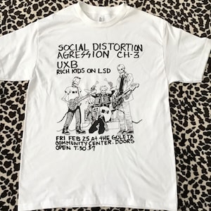 May include: White t-shirt with a black and white illustration of a band called Social Distortion. The text on the shirt reads "Social Distortion Aggression Ch-3 UXB Rich Kids on LSD" and "Fri Feb 25 at the Goleta Community Center. Doors open 7:30. $7."