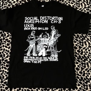 May include: Black t-shirt with a white graphic of a band called "Social Distortion" with the text "Aggression Ch-3, Uxb, Rich Kids on LSD". The graphic also includes the date "Fri Feb 25 at the Goleta Community Center. Doors open 7:30. $7."