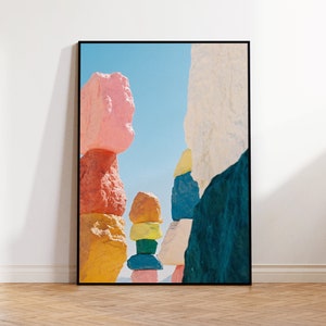 Puede incluir: Una impresión enmarcada de un paisaje abstracto colorido con rocas apiladas pintadas en varios tonos de rosa, naranja, amarillo, azul y blanco sobre un fondo de cielo azul.