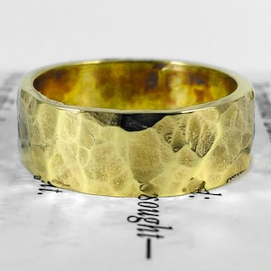 Peut inclure: Une large bague en or avec une texture martelée. La bague est en métal épais et a une surface rugueuse et irrégulière.