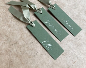 Elegant sage green wedding place name tags with white calligraphy and satin ribbon