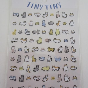 May include: Sheet of stickers featuring various cartoon cat illustrations in different poses and colors. The word "TINY TINY" is written in blue at the top. The stickers are on a clear backing.