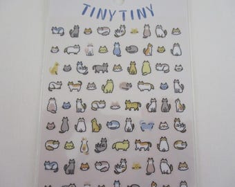 May include: Sheet of stickers featuring various cartoon cat illustrations in different poses and colors. The word "TINY TINY" is written in blue at the top. The stickers are on a clear backing.