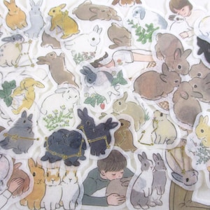 May include: A sheet of stickers featuring various illustrations of rabbits in different poses and colors. The stickers are on a white background and have a translucent, almost watercolor-like appearance.