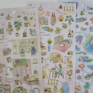 May include: Three sheets of stickers with a pink background and various illustrations. The stickers feature a room tour theme with illustrations of furniture, plants, and other home decor items. The stickers also feature a beach theme with illustrations of palm trees, seashells, and a pool.