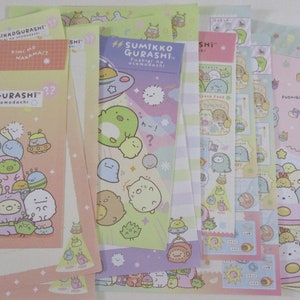 May include: A set of six colorful paper sheets featuring illustrations of cute cartoon characters from the Sumikko Gurashi series. The characters are depicted in various scenes, including a spaceship, a cloud, and a flower. The sheets are printed with the text "Sumikko Gurashi" and "Fushigi na otomodachi" in Japanese.