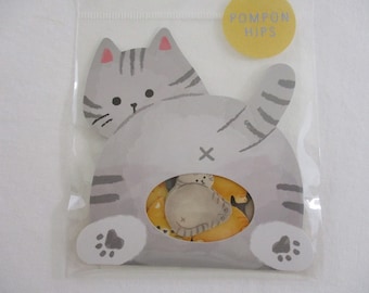 May include: A gray cat with a striped tail and paws, with a yellow circle that says "POMPON HIPS" on the top. The cat's body is cut out to reveal a set of yellow and gray pom-pom stickers.
