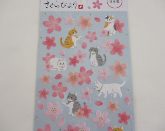 May include: A sheet of stickers featuring adorable cats and pink cherry blossoms. The stickers are on a light blue background with gold glitter accents. The text on the sheet reads "さくらんぼ" and "日本製".