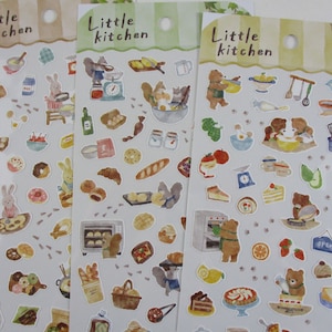 May include: Three sheets of stickers featuring illustrations of animals baking in a kitchen. The stickers are labeled "Little Kitchen" and feature images of bears, squirrels, rabbits, and other animals baking bread, cakes, and pastries. The stickers are perfect for adding a touch of whimsy to your planner, journal, or scrapbook.