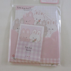May include: A stationery set featuring a pink and white bunny theme. The set includes envelopes, notepaper, and a small notepad, all adorned with cute bunny illustrations and the text "full full bunny". The overall design is soft and pastel-colored.