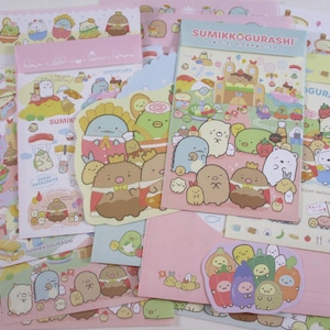 May include: A set of colorful stationery featuring Sumikko Gurashi characters. The stationery includes stickers, memo pads, and letter paper. The characters are all wearing different outfits and are in various poses. The stationery is perfect for adding a touch of fun to your correspondence.