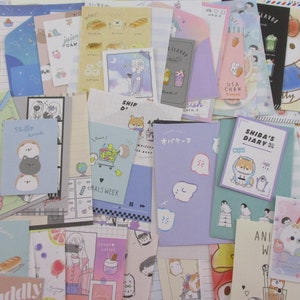 May include: A collection of colorful stationery featuring various illustrations and designs. The stationery includes letter paper, envelopes, and stickers. Some of the designs include a ghost, a dog, a cat, and a hedgehog. The text on the stationery includes "Shiba's Diary", "USA Chan", "Cuddly", and "Omake".