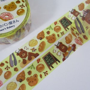 May include: A roll of yellow washi tape with a repeating pattern of brown bears, pastries, and other bakery items. The text on the tape reads "くまのパン屋さん Bear's Bakery".