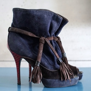 Könnte beinhalten: Ein Paar blaue Wildlederstiefel mit braunen Quasten und einem roten Schlangenlederabsatz. Die Stiefel haben einen umgeschlagenen Schaft und eine offene Zehenpartie.