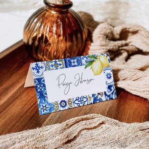 Puede incluir: Una tarjeta de lugar blanca con un borde azul y amarillo con un diseño de limón. La tarjeta dice "Paige Johnson".