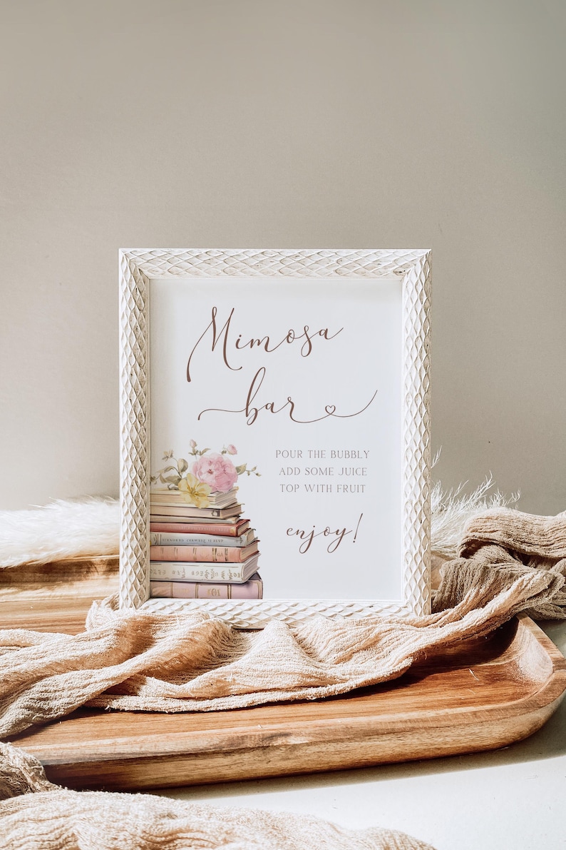 May include: White sign with a brown script font that says "Mimosa Bar" with a small heart. The sign has a watercolor illustration of a stack of books with pink flowers on top. The text below the illustration says "Pour the bubbly, add some juice, top with fruit, enjoy!"