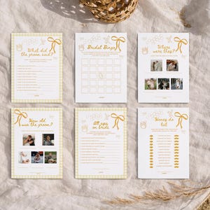 K&ouml;nnte beinhalten: Sechs Hochzeitsspielkarten mit gelb-wei&szlig;em Vichy-Rand und goldenem Text. Die Spiele umfassen "Was hat der Br&auml;utigam gesagt?", "Hochzeitsbingo" und "Honey do list". Die Karten sind auf einer wei&szlig;en Oberfl&auml;che angeordnet.