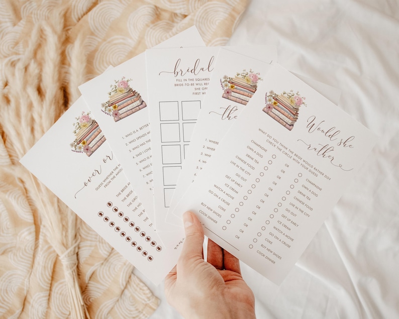 May include: A set of bridal shower game cards with a book stack and floral design. The cards include "Would She Rather", "Bridal Bingo", and "Never Have I Ever".
