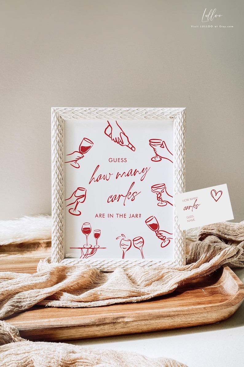 May include: White framed sign with red text and illustrations. The sign reads "Guess how many corks are in the jar?" and features drawings of hands holding wine glasses. A small card with the same text and a heart is also present.