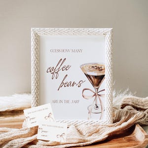 May include: A white framed sign with the text "GUESS HOW MANY coffee beans ARE IN THE JAR?" and a watercolor illustration of a martini glass filled with coffee beans. Two white cards with the text "HOW MANY COFFEE BEANS guess: name:" are on a wooden surface.