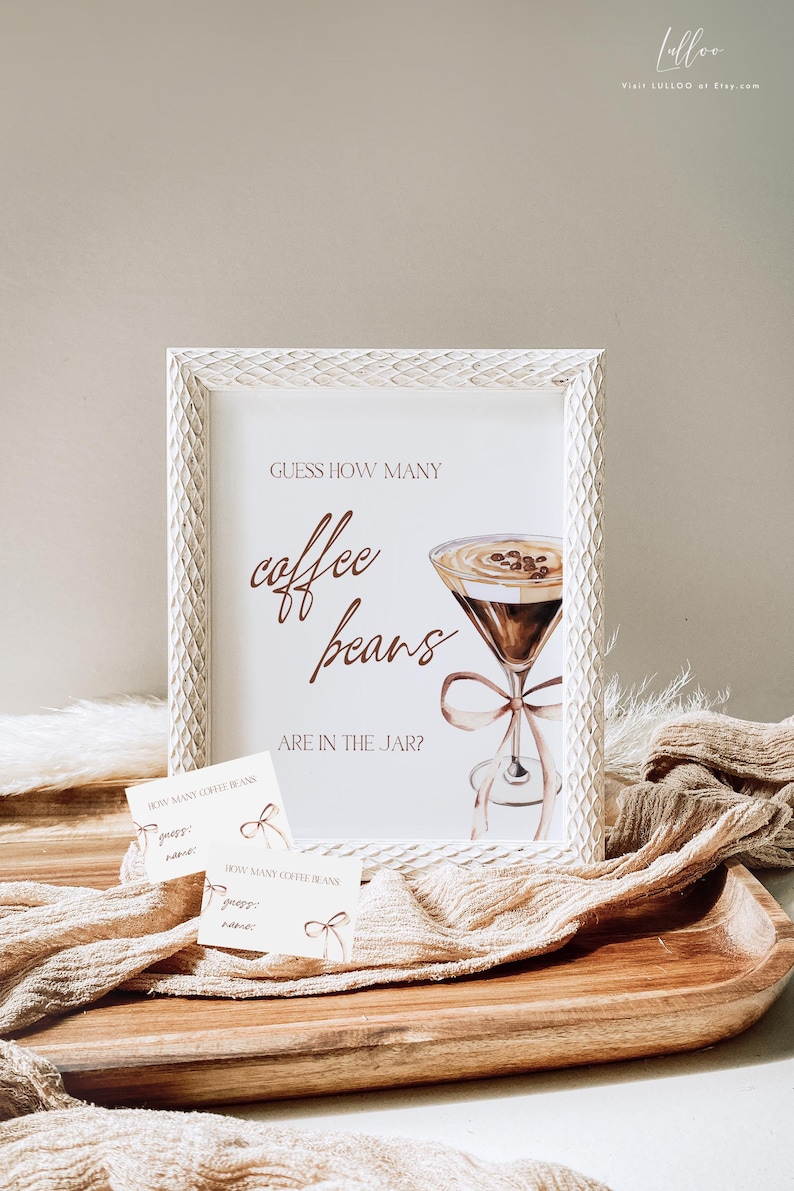 May include: A white framed sign with the text "GUESS HOW MANY coffee beans ARE IN THE JAR?" and a watercolor illustration of a martini glass filled with coffee beans. Two white cards with the text "HOW MANY COFFEE BEANS guess: name:" are on a wooden surface.