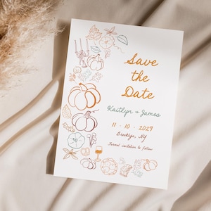 以下が含まれることがあります： カボチャ、葉、そして「Save the Date」のテキストが特徴の、秋をテーマにしたデザインの白いカード。「Kaitlyn + James」の名前と日付「11.10.2029」も含まれています。カードはニュートラルな質感の背景に置かれています。