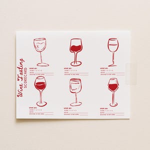 May include: A white wine tasting scorecard featuring six red wine glass illustrations. The card has spaces for scores and notes, with the words "Wine Tasting Scorecard" printed vertically on the left side.