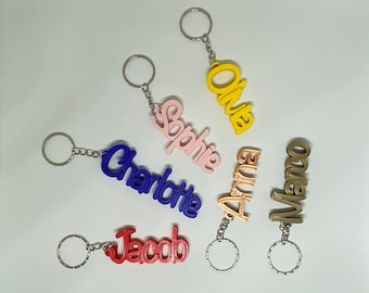 May include: Six colorful keychains with names written on them. The names are Olivia, Sophie, Charlotte, Anna, Marco, and Jacob. The keychains are made of plastic and have a silver metal ring.