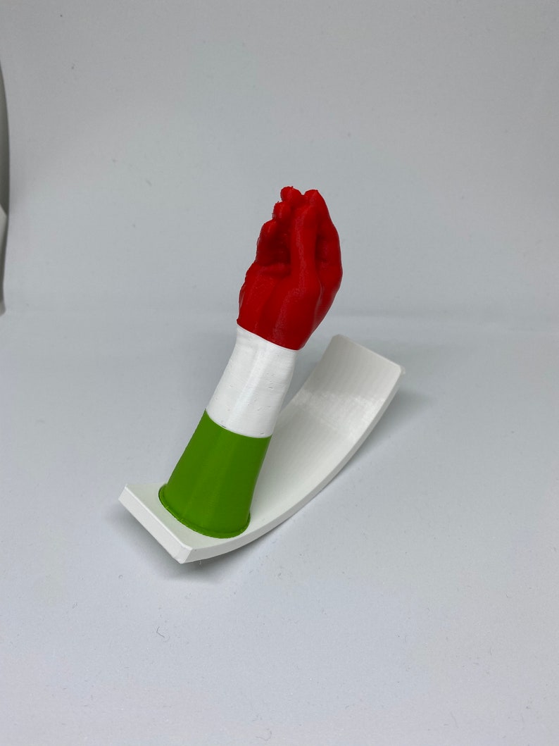 K&ouml;nnte beinhalten: Eine 3D-gedruckte Handskulptur, die in den Farben der italienischen Flagge bemalt ist. Die Hand macht eine Geste mit ausgestreckten Fingern und eingezogenem Daumen. Die Skulptur ist auf einem wei&szlig;en Sockel montiert.