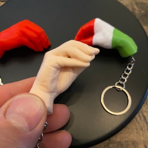 Peut inclure: Un porte-cl&eacute;s avec une petite figurine de main tenant un drapeau italien miniature. Le drapeau est rouge, blanc et vert. Le porte-cl&eacute;s est en m&eacute;tal et a un anneau argent&eacute;.