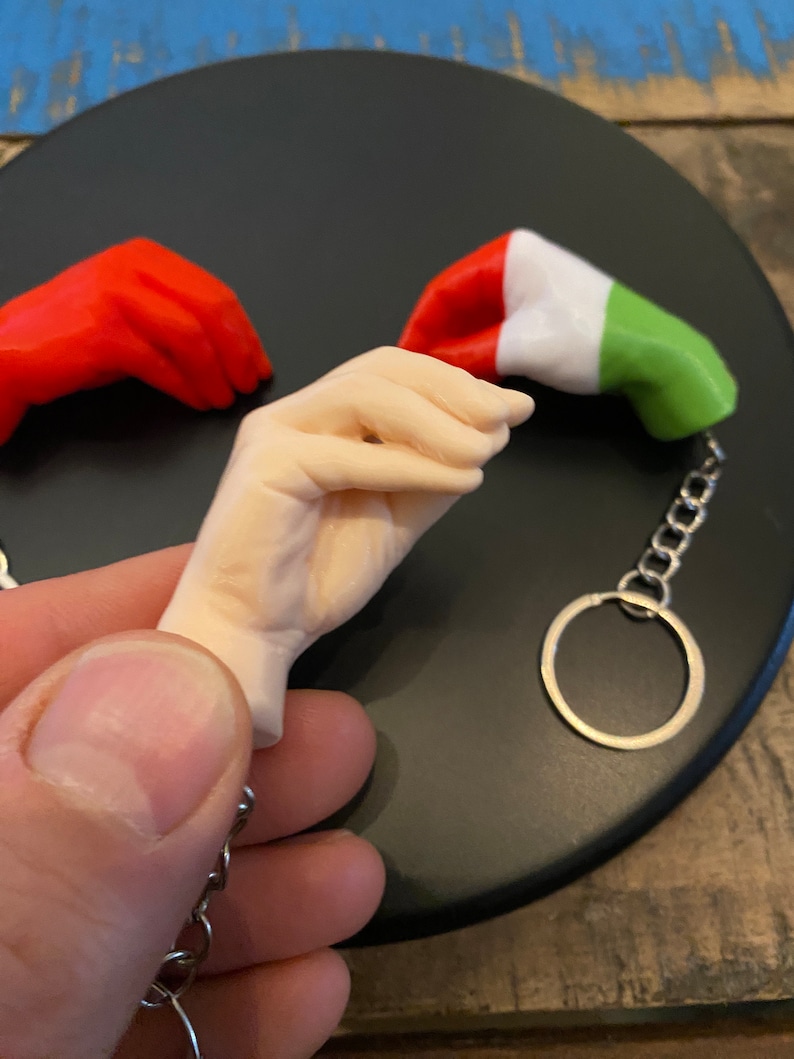 Peut inclure: Un porte-cl&eacute;s avec une petite figurine de main tenant un drapeau italien miniature. Le drapeau est rouge, blanc et vert. Le porte-cl&eacute;s est en m&eacute;tal et a un anneau argent&eacute;.