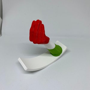 K&ouml;nnte beinhalten: Eine rote, 3D-gedruckte Handskulptur mit einem gr&uuml;n-wei&szlig;en Sockel. Die Hand ist in Fauststellung.