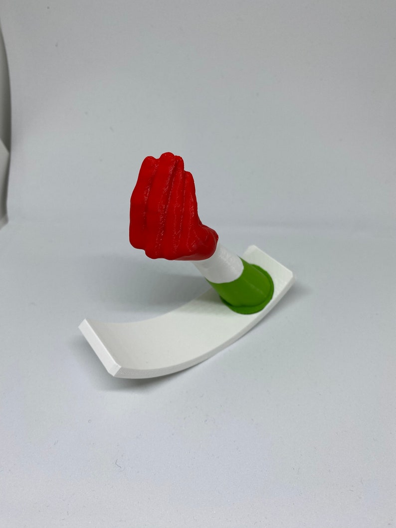 K&ouml;nnte beinhalten: Eine rote, 3D-gedruckte Handskulptur mit einem gr&uuml;n-wei&szlig;en Sockel. Die Hand ist in Fauststellung.