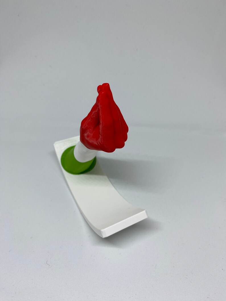 K&ouml;nnte beinhalten: Eine rote 3D-gedruckte Handskulptur in der italienischen Handgeste "mano fico" oder "figa". Die Hand ist auf einem wei&szlig;en und gr&uuml;nen Sockel montiert.
