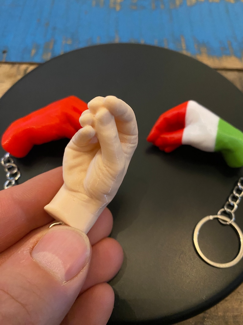 Peut inclure: Trois porte-cl&eacute;s repr&eacute;sentant une main, une main rouge et une main aux couleurs du drapeau italien. Les porte-cl&eacute;s sont en mat&eacute;riau blanc lisse.
