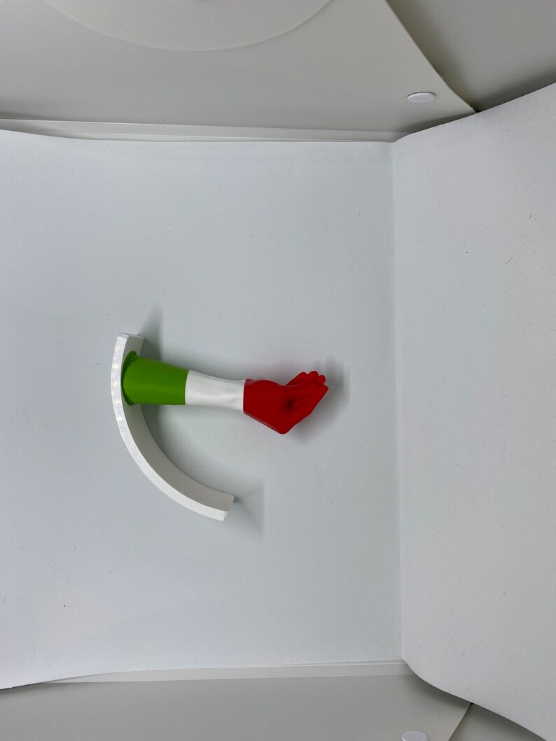 K&ouml;nnte beinhalten: Eine kleine, handf&ouml;rmige Figur mit einem gr&uuml;n-wei&szlig;-roten Farbschema, das an die italienische Flagge erinnert. Die Figur ist mit ausgestreckten Fingern posiert, als w&uuml;rde sie eine Geste machen.