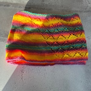 May include: A colorful knitted headband with a striped pattern in shades of yellow, orange, red, purple, and green. The headband has a lacy design.