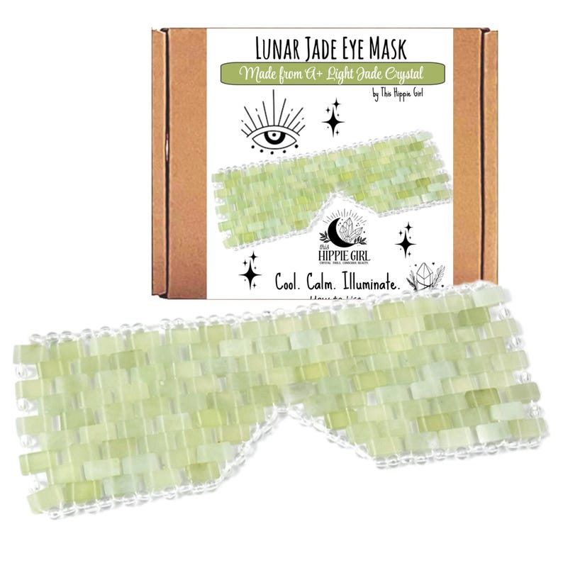 May include: A light green Lunar Jade eye mask made from A+ light jade crystal. The mask is made of small, rectangular jade pieces and has a white border. The packaging is a brown box with text that reads "Lunar Jade Eye Mask" and "Cool. Calm. Illuminate."